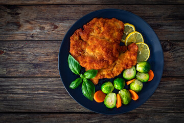 Crispy breaded chicken cutlet with boiled carrot and Brussels sprouts on wooden table. Top view	