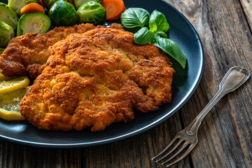 Crispy breaded chicken cutlet with boiled carrot and Brussels sprouts on wooden table