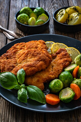 Crispy breaded chicken cutlet with boiled carrot and Brussels sprouts on wooden table