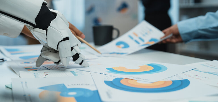 A human and robot collaborate in an office setting, analyzing colorful charts and reports. This image represents the future of teamwork and data-driven decision-making in business.Noogenesis
