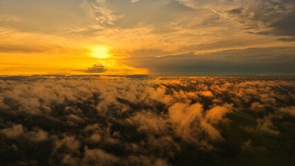 A high-altitude aerial photograph capturing a sunrise above a vast forest with golden morning mist drifting through the treetops