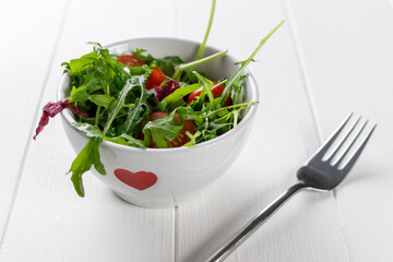 Fresh Mixed Salad in Heart Bowl on White Table with Fork: Healthy Spring Meal Concept
