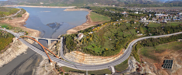 Aerial panorama of Kukës showing the A1 bridges, lake shoreline, and surrounding hills in warm autumn tones.