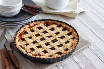 Freshly baked lattice pie on a rustic table beside stacked plates, bowls, and a white teapot, creating a cozy homemade dessert scene.