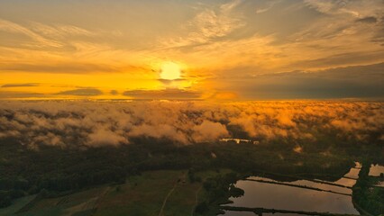 A high-altitude aerial photograph capturing a sunrise above a vast forest with golden morning mist drifting through the treetops