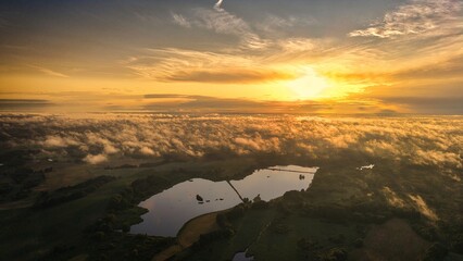 A high-altitude aerial photograph capturing a sunrise above a vast forest with golden morning mist drifting through the treetops