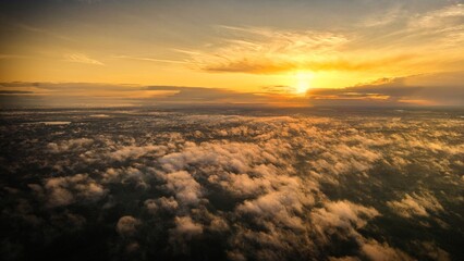 A high-altitude aerial photograph capturing a sunrise above a vast forest with golden morning mist drifting through the treetops