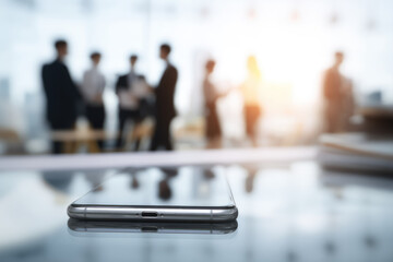 Smartphone on glass table with blurred businesspeople in background modern office teamwork communication technology and professional atmosphere soft sunlight focus on device