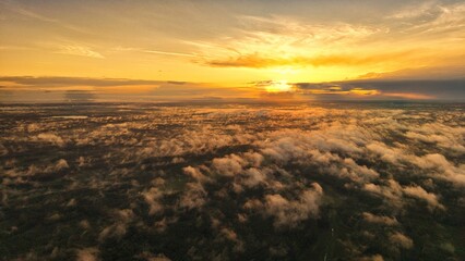 A high-altitude aerial photograph capturing a sunrise above a vast forest with golden morning mist drifting through the treetops