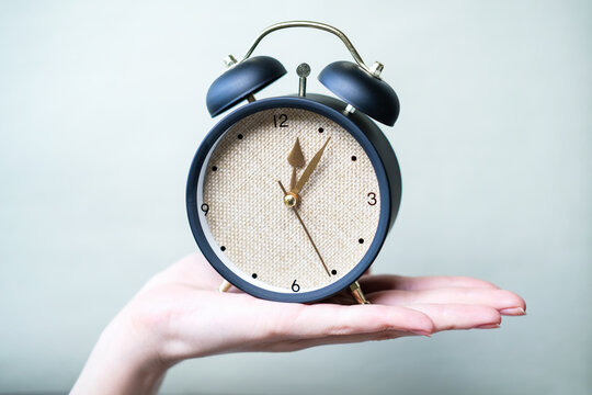 Female hand holding alarm clock on gray background.