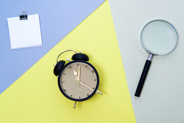 Magnifying glass, alarm clock and blank paper on color background.