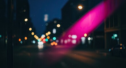 Atmospheric out-of-focus view of a city street at night with colorful bokeh lights and a vibrant pink light flare, creating a dreamy and moody urban background