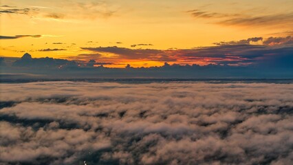 A high-altitude aerial photograph capturing a sunrise above a vast forest with golden morning mist drifting through the treetops