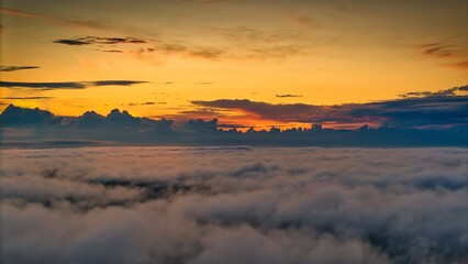A high-altitude aerial photograph capturing a sunrise above a vast forest with golden morning mist drifting through the treetops