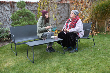 Two people sharing a conversation on outdoor benches in an autumn garden setting
