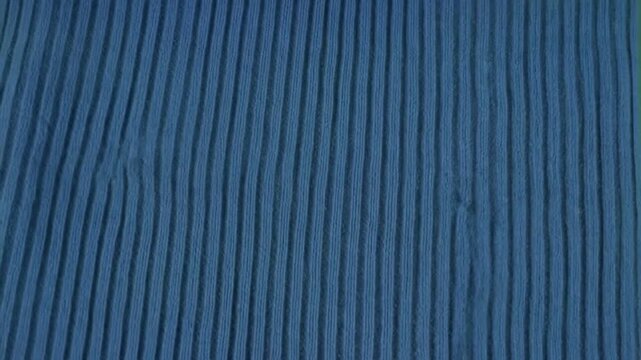 Close up of a blue knitted scarf draped on a green background.