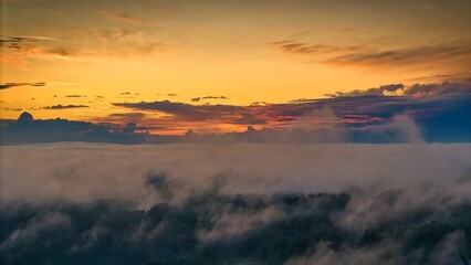A high-altitude aerial photograph capturing a sunrise above a vast forest with golden morning mist drifting through the treetops