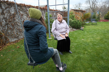 Naklejka premium Intergenerational connection: young and elderly enjoying swing time in autumn garden