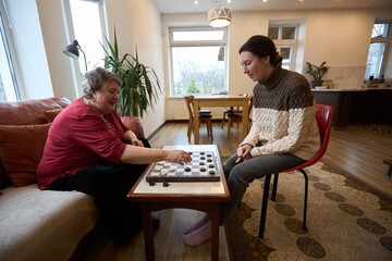 Grandmother and granddaughter enjoy a game of checkers in cozy living room setting