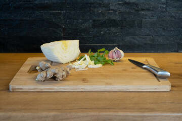 Fresh ingredients on a wooden board, cabbage, ginger, garlic, and herbs, creating a warm and natural cooking atmosphere.