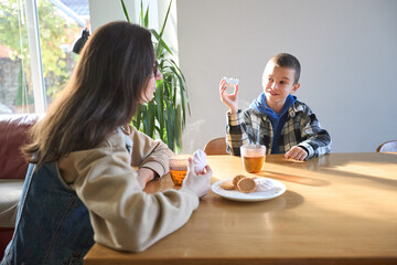 Family breakfast: mother and son sharing cookies and tea in bright kitchen morning