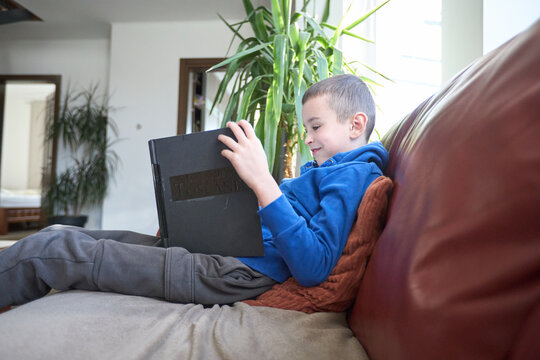 Young boy reading a large book on a couch in a cozy living room setting