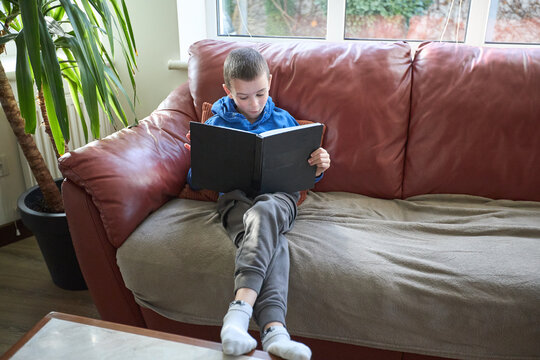Young boy relaxing on sofa reading a book at home