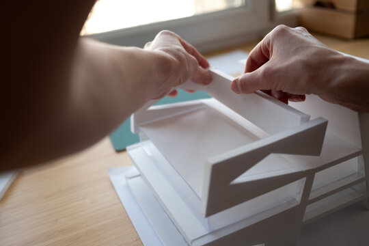 Close-up of an architect's hands building a white scale model. A concept for creativity, design, engineering, and construction projects.