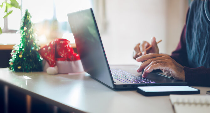 close up shot, asian man using laptop working and decoration christmas background with red hat, christmas tree on desk, working on christmas holiday concept - Powered by Adobe