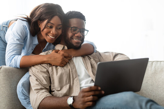 A relaxed African American couple sits closely on their sofa, sharing a digital tablet.