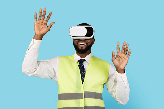 Excited Black Builder Man Wearing VR Glasses Standing On Blue Background, African American Male Construction Manager Enjoying Virtual Reality Experience And Playing Video Games, Closeup
