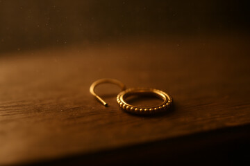 Gold Earring Resting On Wooden Table In Warm Atmospheric Light