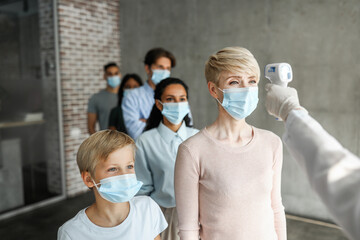 Multiracial group of patients different ages in protective face masks checking body temperature with electronic thermometer before vaccination against coronavirus at clinic or immunization center