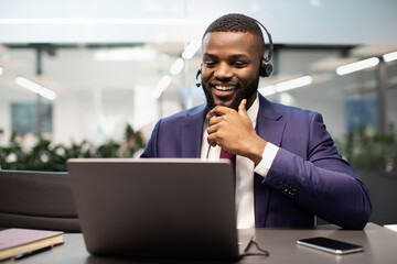 Happy african american guy manager having video call at office, using headset and modern laptop, attending online conference or having video chat with business partners, copy space
