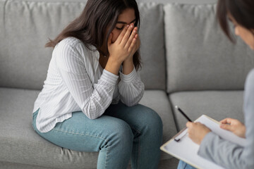 Obraz premium A woman sits on a sofa, crying and grieving while discussing her feelings with a psychologist. She shows signs of stress and depression in a mental health clinic setting.