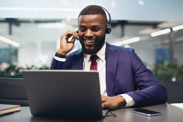 Cheerful african american manager having video call at office, using headset and modern laptop, attending online conference or having video chat with business partner, copy space
