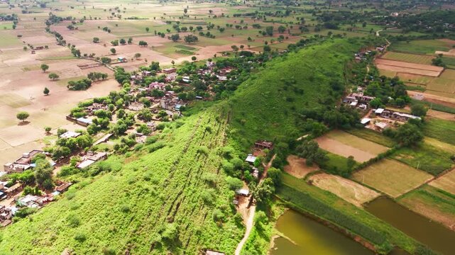 A peaceful village nestled in the Aravalli mountains of Rajasthan, showing small houses, natural slopes, and a calm rural landscape captured from a wide drone view.
