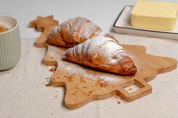 Studio shot of croissants served on a tree-shaped board with a block of fresh butter and coffee.