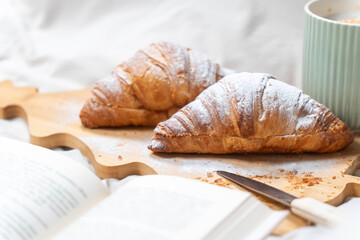 Two croissants on a tree-shaped board with a coffee cup and open book, depicting a slow holiday morning.