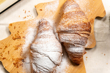 Overhead flat lay of two golden croissants dusted with powdered sugar on a wooden Christmas tree board.