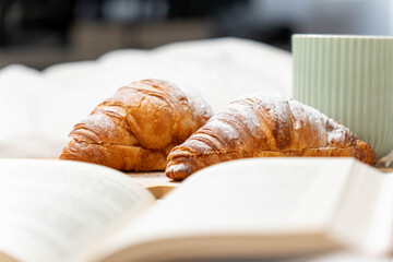 Eye-level view of sugar-dusted croissants and an open book, capturing the essence of a lazy weekend morning.