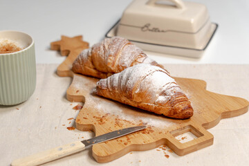 Classic french breakfast featuring croissants on a wooden board, a butter dish, and a frothy cappuccino.