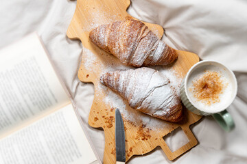 Vertical flat lay of croissants, coffee, and a book on a Christmas tree board, perfect for holiday blogs.