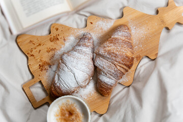 Top-down view of a romantic breakfast setup with croissants and coffee on rumpled white bed sheets.