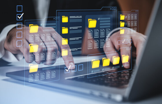Businessman managing digital folders and files through transparent interface on laptop, representing data organization and technology concept.