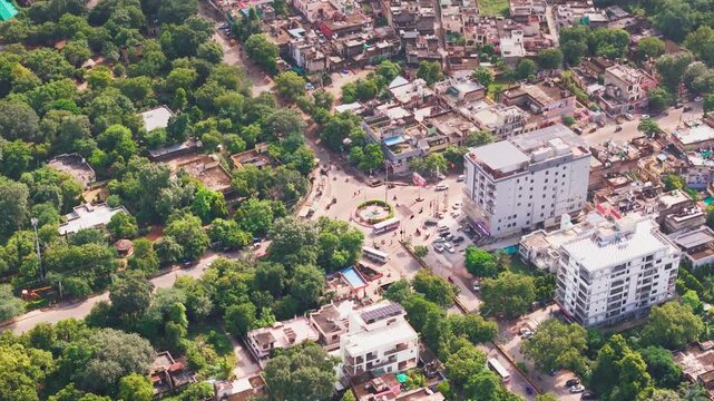 Bright daylight drone view of Alwar city with organized streets, clusters of homes, natural greenery, and light traffic movement.