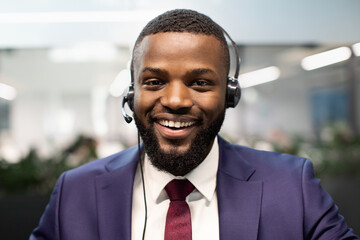 Closeup portrait of smiling handsome young african american man in blue suit using headset, businessman having video conference with business partners or doing job interview online