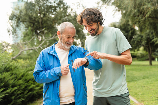 Senior father and son jogging doing sport together, checking cardio levels using smartwatch app after running in the morning