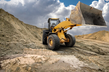 A large loader is lifting dirt at a construction site surrounded by mounds of soil under a dramatic...