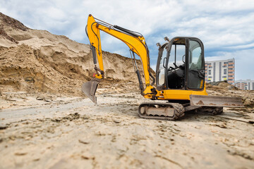 Obraz premium An excavator works to clear sand at a construction site surrounded by tall buildings under a cloudy sky, showcasing urban development activities